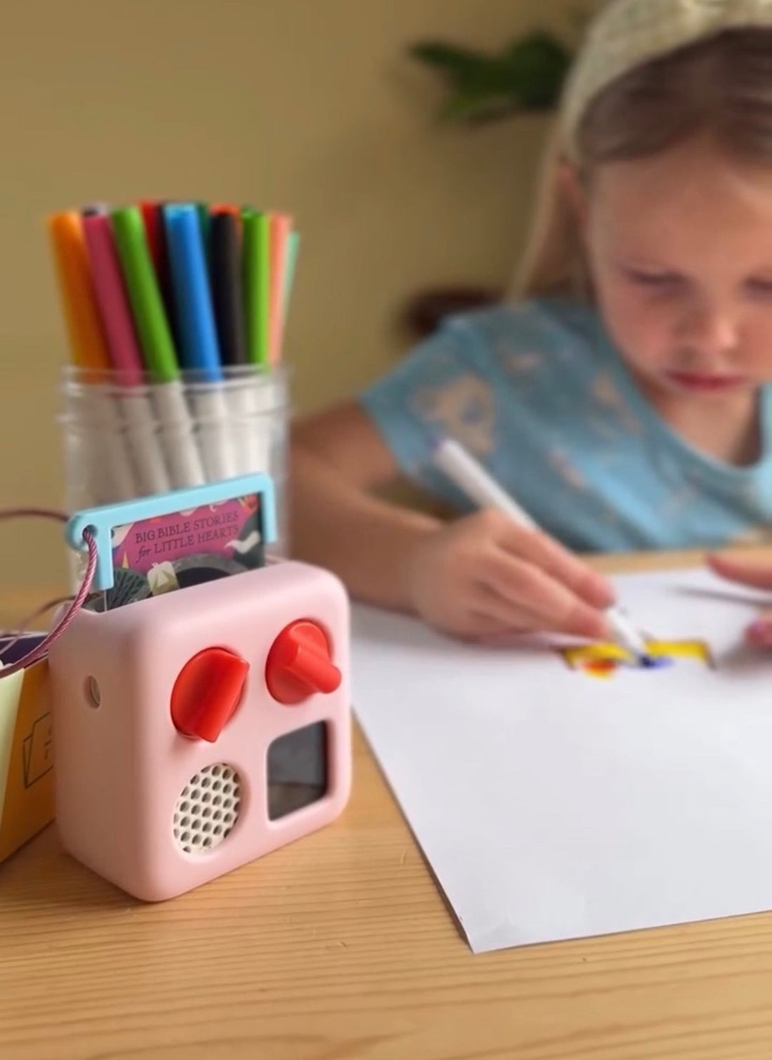 Young girl coloring while listening to a Big Bible Stories Christian audio card on a Yoto Mini, showing how Bible stories can be enjoyed during quiet time and creative play.